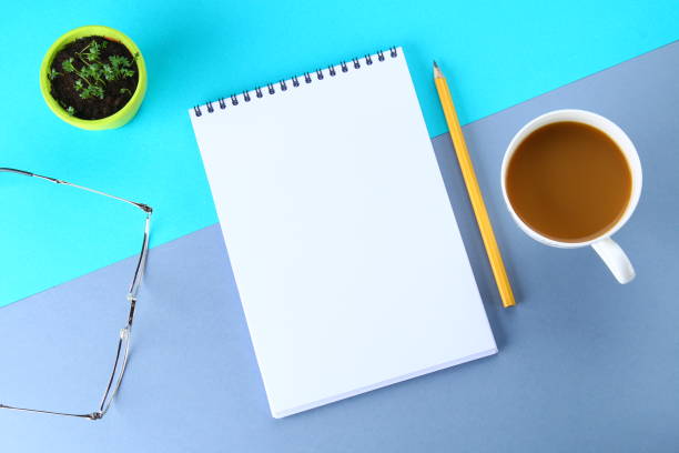 istock Top view image of open notebook with blank pages and coffee on blue background, ready for adding or mock up. Still life, business, office supplies or education concept. 919372044