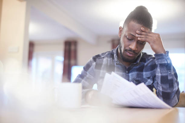 preocupado el joven hombre lectura a través de estados de cuenta bancarios - financial burden fotografías e imágenes de stock