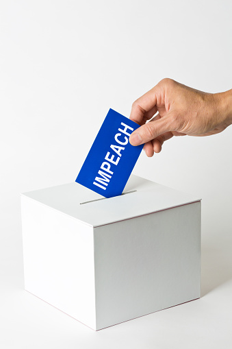 A hand inserting a vote ballet into a voting box for a vote to impeach the government and or officials