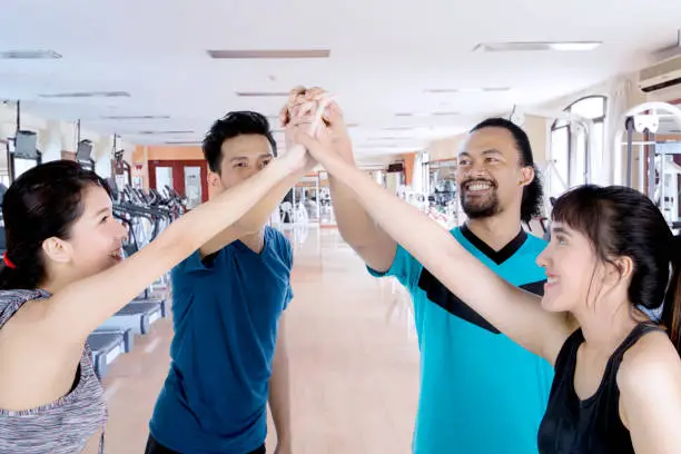 Four young people making high five hand gesture before doing a workout in the gym center
