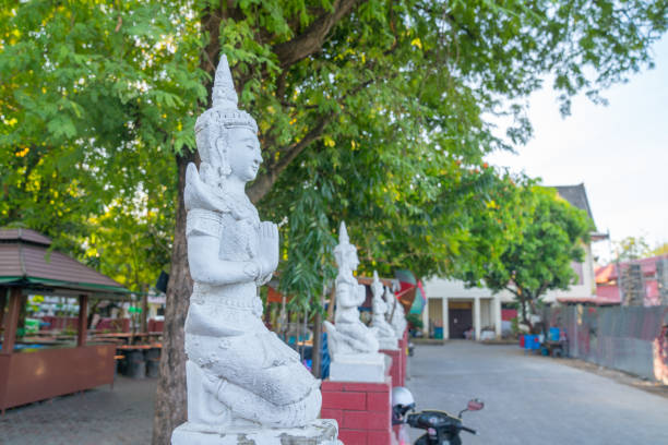 Line of white Buddha image statues lining one side of a short road.