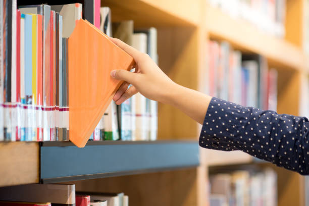 istock male hand choosing and picking orange book in public library 919470984