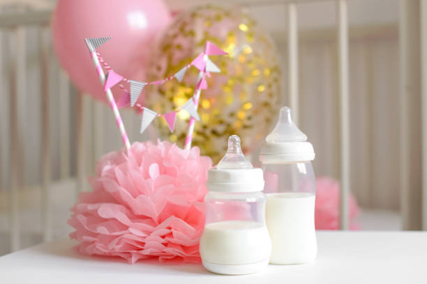 babyflaschen mit muttermilch mit verschiedenen festlichen papier dekor und luftballons vor babyzimmer. es ist ein mädchen oder baby geburtstag feier-konzept. baby-dusche-konzept. - baby congratulating toy birthday stock-fotos und bilder