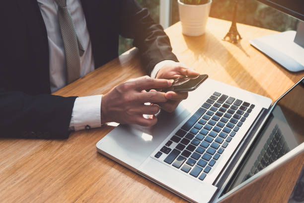 istock Businessman using smartphone and laptop computer at workplace sitting update or report in email application earnings with network 919530732