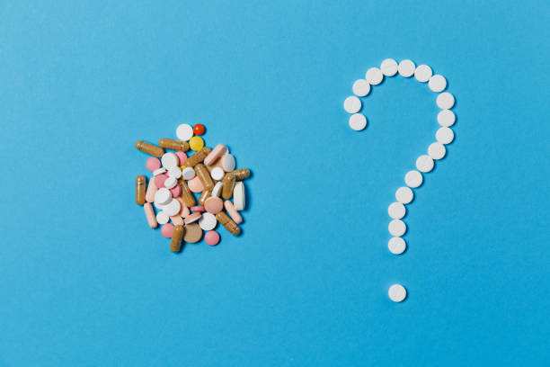 istock Medication white round tablets arranged in question mark shape isolated on blue color background. Bunch of multicolored pills, colorful sign. Concept of health, treatment, choice, healthy lifestyle. 919538956
