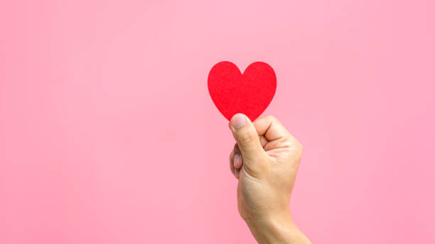 istock Hand holding a red fabric heart in a pink background. 919560878