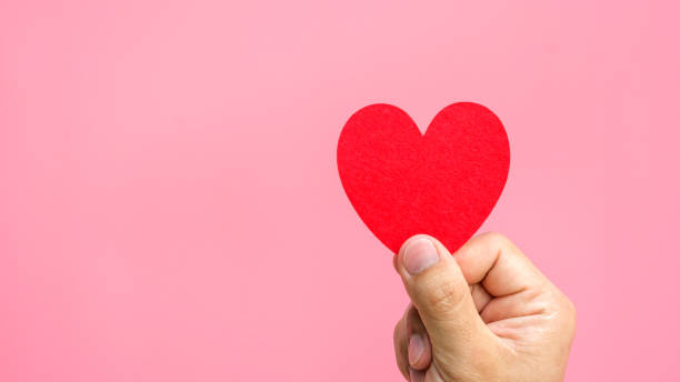 istock Hand holding a red fabric heart in a pink background. 919561350