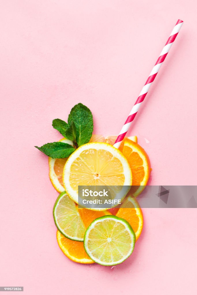 Funny juice concept Glass of juice made of citrus slices with mint leaves and a straw on light pink background. Citrus juice concept Summer Stock Photo