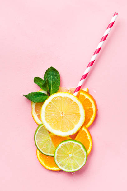 Funny juice concept Glass of juice made of citrus slices with mint leaves and a straw on light pink background. Citrus juice concept cooling down photos stock pictures, royalty-free photos & images