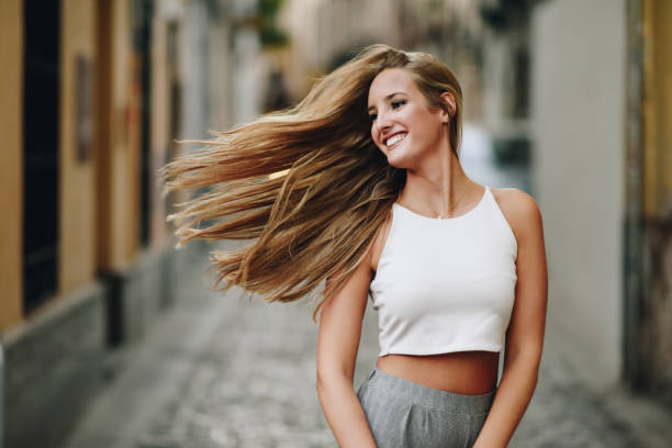 giovane donna felice con i capelli in movimento in ambiente urbano. - blond hair fashion smiling attractive female foto e immagini stock