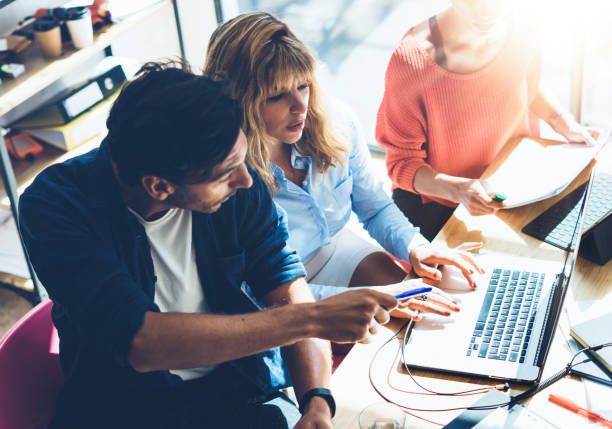 istock Teamwork process concept.Young coworkers team work with new startup project in office.Analyze document, plans.Modern laptop on wood table, papers, documents.Horizontal, blurred background. 919605372