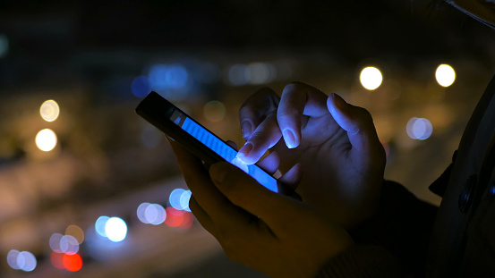 Close-up shot of woman hands with smartphone in the city at night. Technology, winter and holiday concept