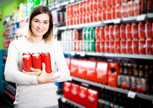 Young woman choosing cold beer in supermarket