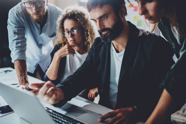 istock Coworkers working together in modern office.Bearded man talking with colleague and using laptop while sitting at the wooden table.Horizontal.Blurred background. 919644254
