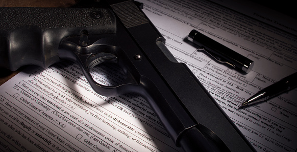 Black handgun and background check paperwork with dishonorable discharge clause obvious