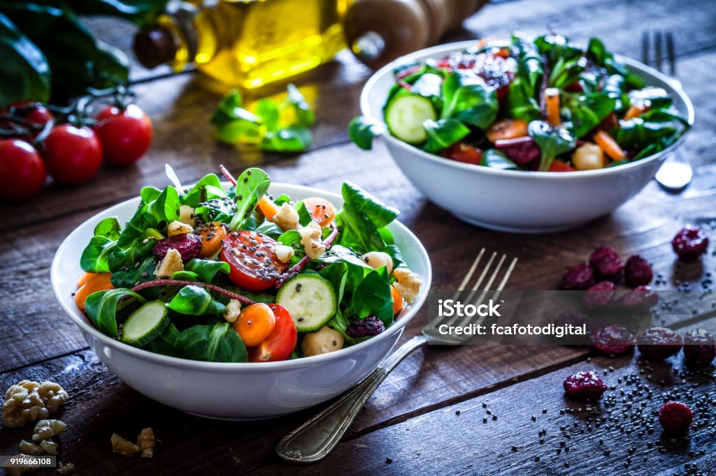 Two fresh salad bowls Two healthy salad bowls with chia seeds shot on rustic wooden table. The ingredients included for the preparation are chia seeds, lettuce, cherry tomato, carrot, arugula, cucumber and avocado. Some vegetables for salad preparation are scattered on the table. DSRL studio photo taken with Canon EOS 5D Mk II and Canon EF 100mm f/2.8L Macro IS USM Salad Stock Photo