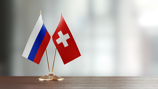 Russian and Swiss flag pair on desk over defocused background. Horizontal composition with copy space and selective focus.