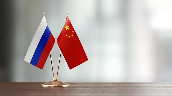 Russian and Chinese flag pair on desk over defocused background. Horizontal composition with copy space and selective focus.