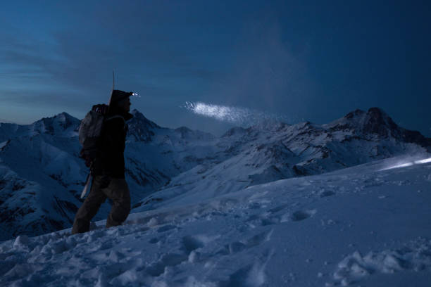 istock Brave traveler man commit ski tour on high mountain at night. Professional snowboarder lights the way with a headlamp. Backcountry in great winter snowy mountains. Wearing backpack 919758864