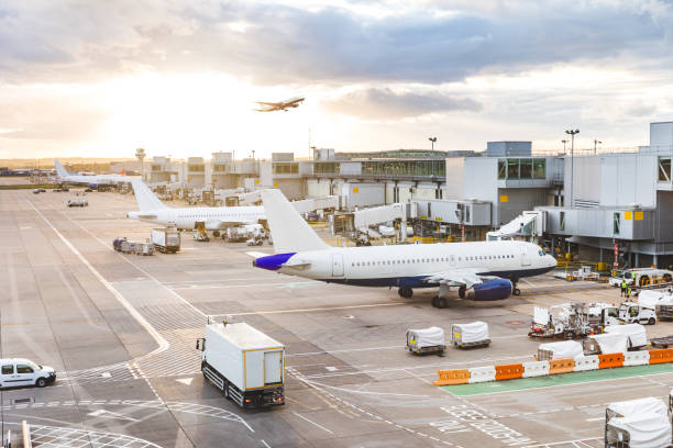 Busy airport view with airplanes and service vehicles at sunset Busy airport view with airplanes and service vehicles at sunset. London airport with aircrafts at gates and taking off, trucks all around and sun setting on background. Travel and industry concepts airports stock pictures, royalty-free photos & images