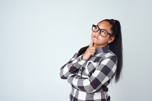 Studio shot of a cute young girl looking thoughtful against a gray background