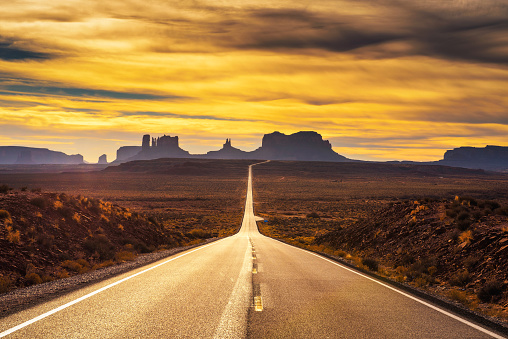Desert road leading to Monument Valley photographed at the Forrest Gump Point with dramatic sunset sky.