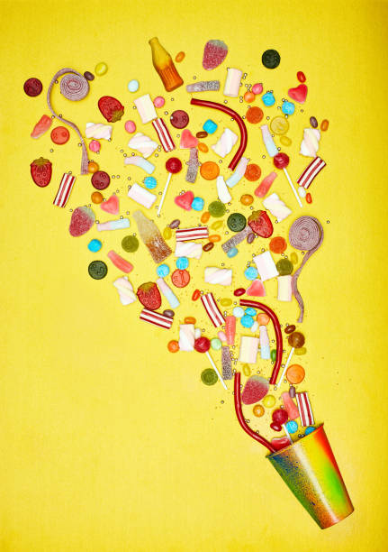 Different candies spilled out of paper cup on yellow background
