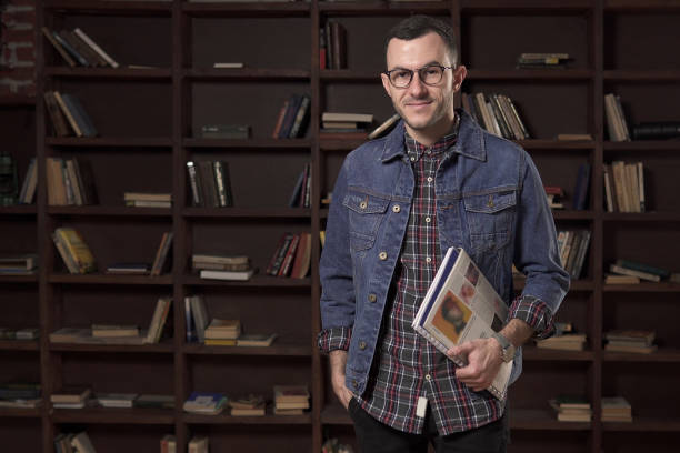 istock Young happy man student holding book in front of the bookcase 919830028