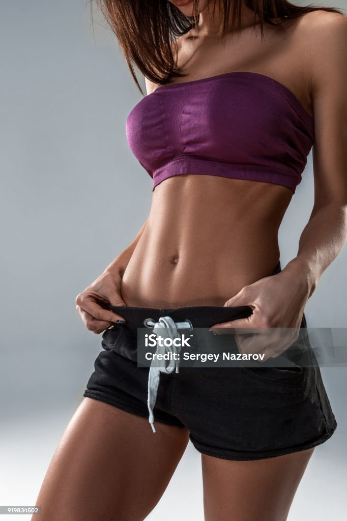 Primo piano di uno stomaco ben curato e stretto di una giovane donna su uno sfondo grigio - Foto stock royalty-free di Accudire