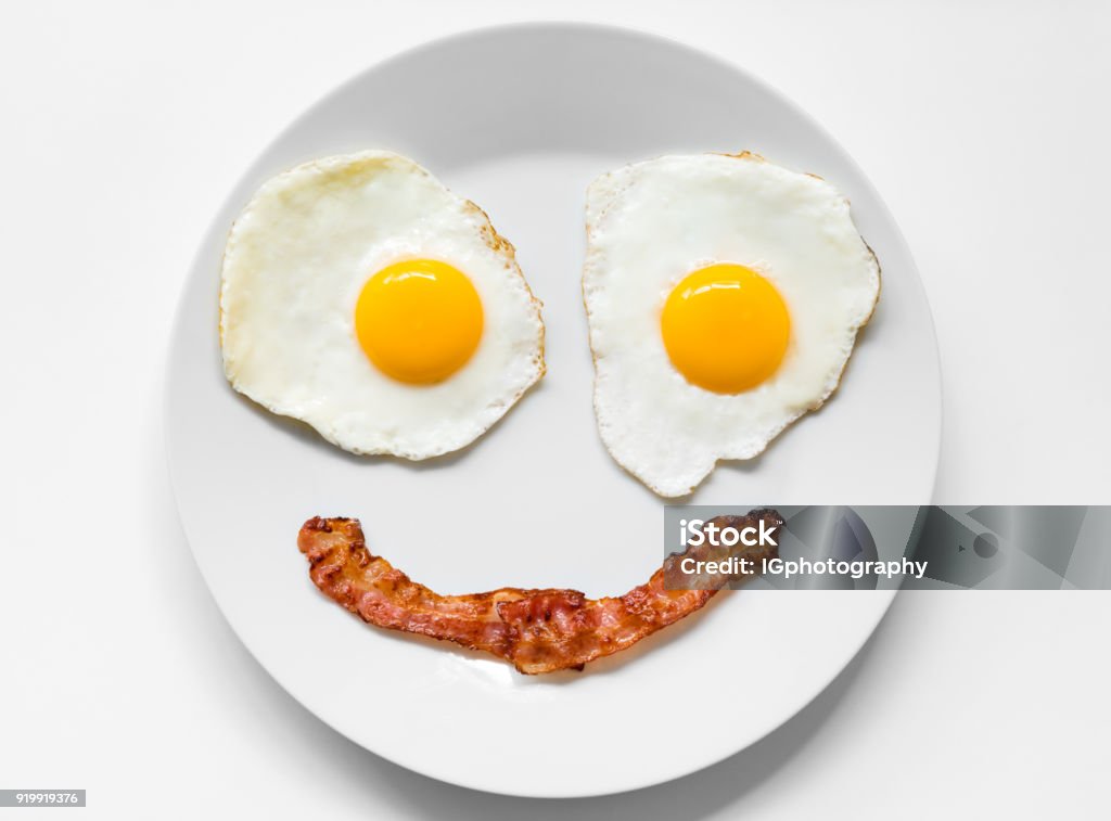 Smiling and Positive Face made from Fried Eggs and Bacon on Plate Smiling and positive face made from fried eggs and bacon on plate. This is the typical breakfast in a low-carb high-fat Keto (Ketogenic) or Paleo diet which can help with weight loss and overall well being. Animal Egg Stock Photo