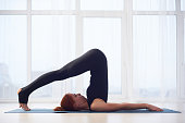 Beautiful young woman practices yoga asana Halasana Plough pose in the yoga studio.