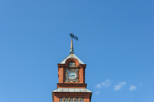 the tower is of red brick with a clock decorated with ceramic tiles on the background of blue sky