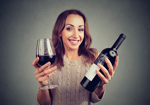 Young woman holding glass of wine and bottle looking happily at camera enjoying taste.