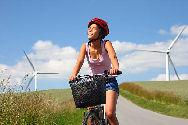 Young beautiful woman riding bicycle in countryside. She is wearing backpack and sunglasses. Spreading arms, having fun. It\
