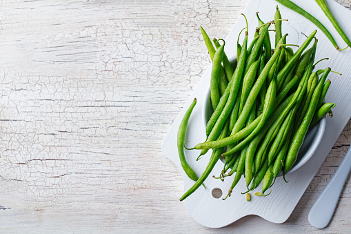 Green beans in white bowl on cutting board. Top view. Copy space.