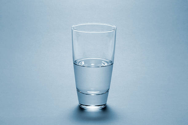 Half full water glass over blue background stock photo