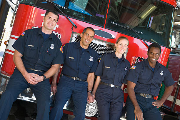 Firefighters standing by a fire engine Portrait of firefighters standing by a fire engine fire station stock pictures, royalty-free photos & images