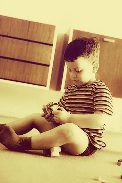 vintage sepia toned  image of a cute kid focused in his play at home.