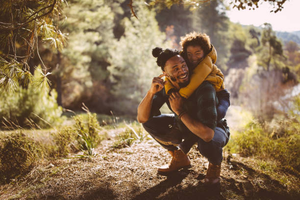 padre e hijo divertirse con piggyback ride en bosque - actividad de fin de semana fotos fotografías e imágenes de stock