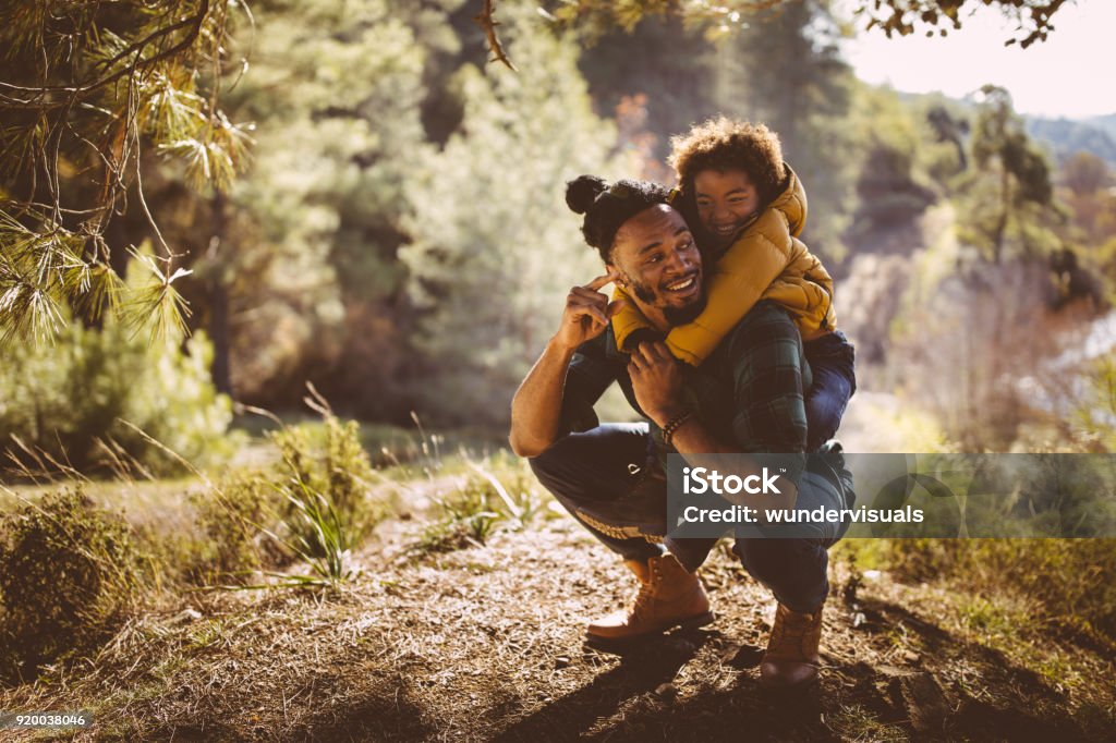 Father and son having fun with piggyback ride in forest Dad and son bonding and having fun with piggyback ride on mountain hiking adventure Family Stock Photo