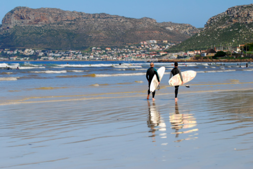 A small wave feathers and breaks at Long Beach, in Kommetjie, Cape Town, with the mountains of Table Mountain National Park in the background.