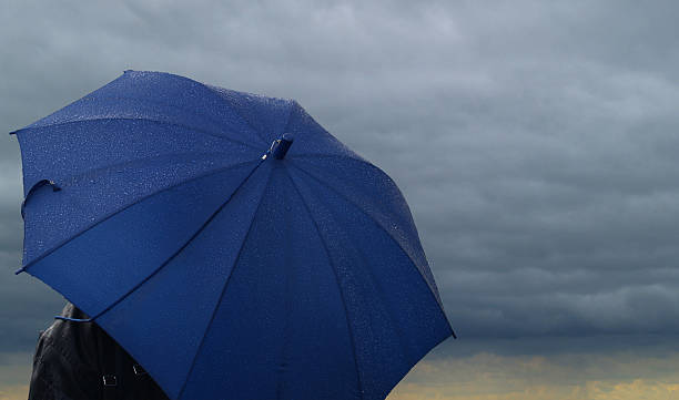 Blue umbrella over a dark stormy cloud stock photo