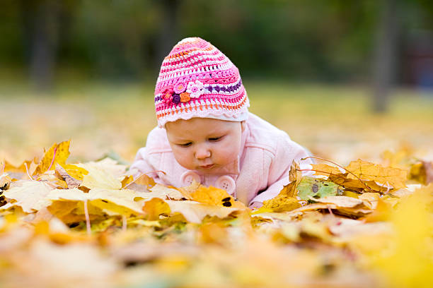 Portrait of a cute baby girl lying on autumn leaves in the public park.