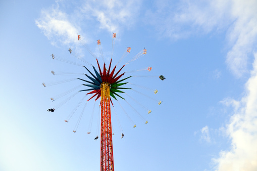Amusement park carousel: Modern Chain Swing Ride tower, from below, people fly in their seats  in a blue cloudy sky. Horizontal orientation.