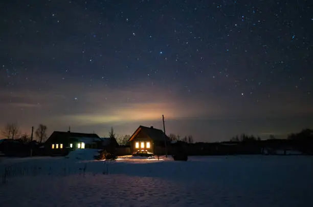 Photo of Houses in the Russian village. Winter, frosty night. Starry sky over the roofs of houses.