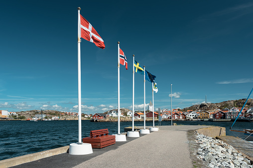 Flags of scandinavian countries waving on flagpoles on the shore. Blue sky over th eflags. View at the Scandinavian coastal city.