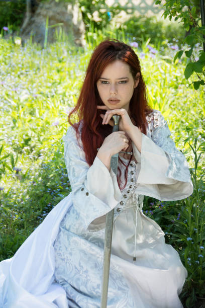 istock Red headed woman kneeling in garden with sword, three quarter length. 920196586