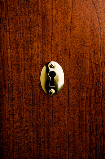 Brass keyhole on a wooden background.