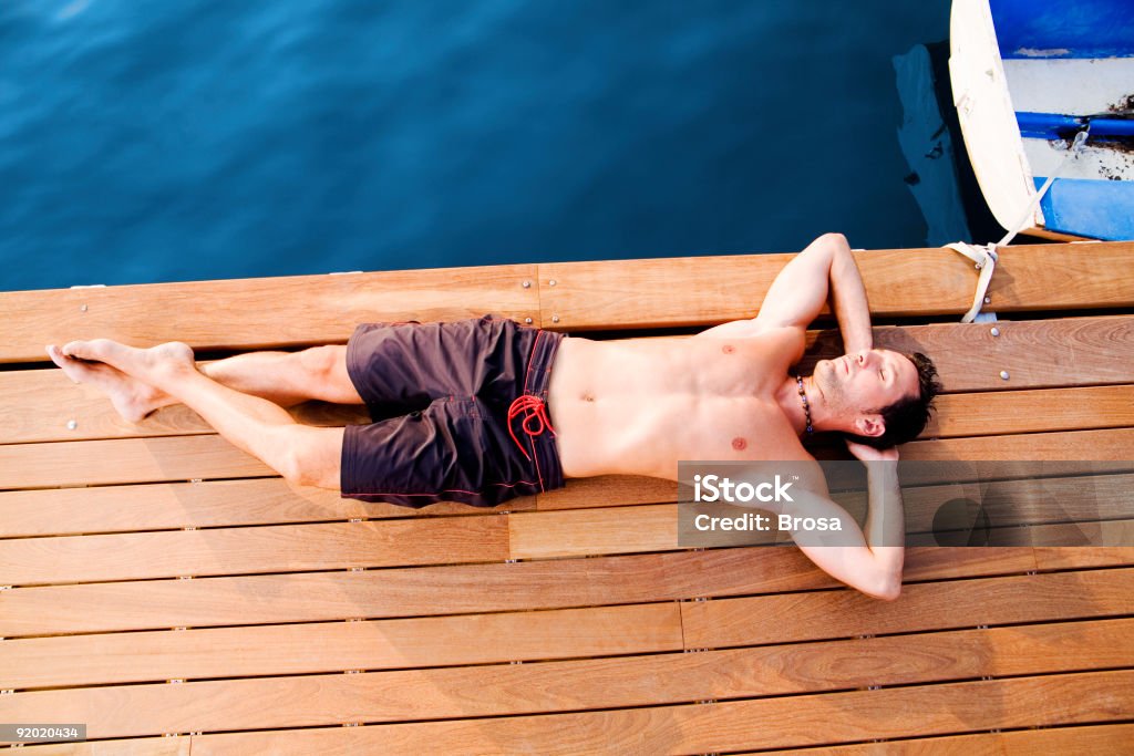 A man relaxing on a wooden deck by the pool Handsome young man lying on the dock. 20-24 Years Stock Photo