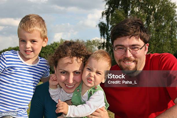 Famiglia Con Due Bambini Sul Prato E Alberi In Primo Piano - Fotografie stock e altre immagini di Accudire